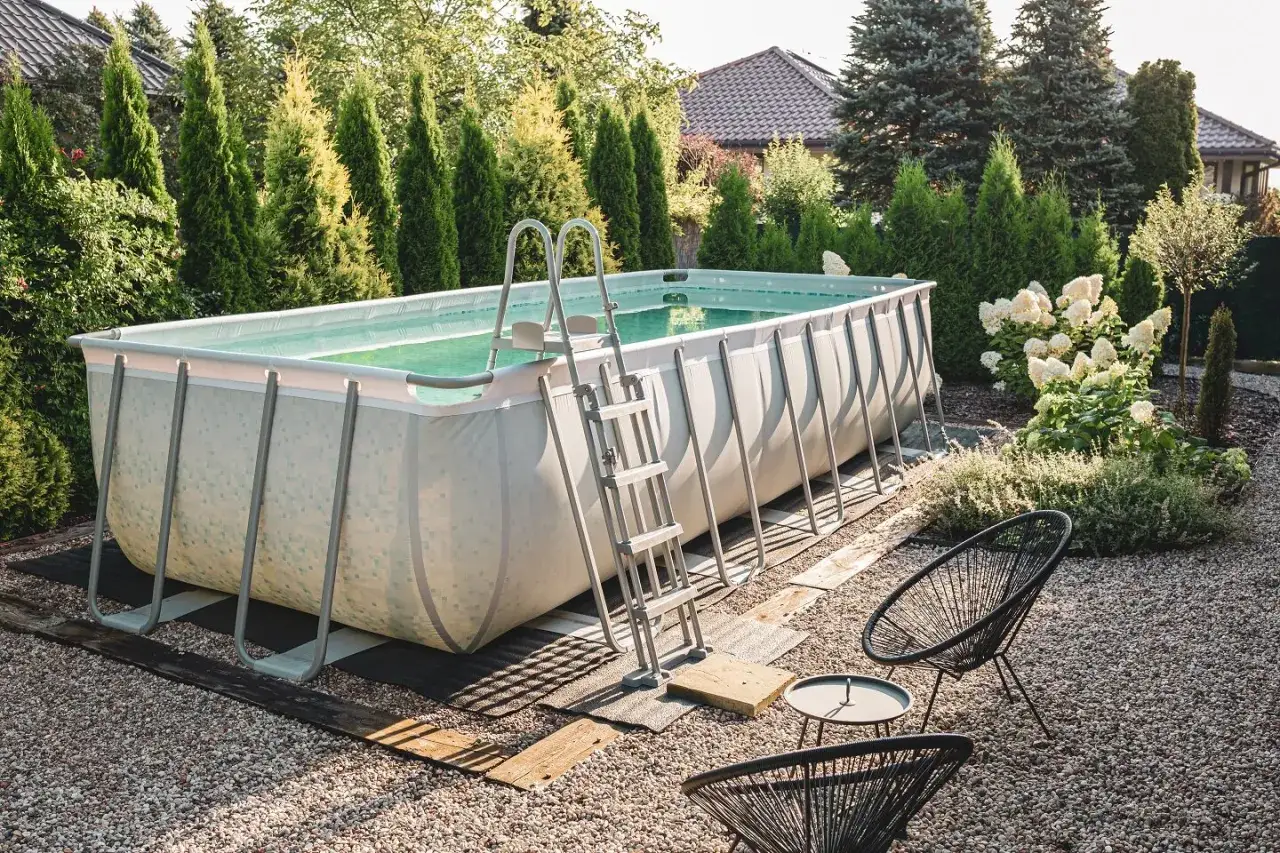 Fertig, den **Pool aufstellen** war erfolgreich! Ein rechteckiger Stahlrahmenpool mit Leiter steht im Garten, umgeben von Zypressen und Hortensien.