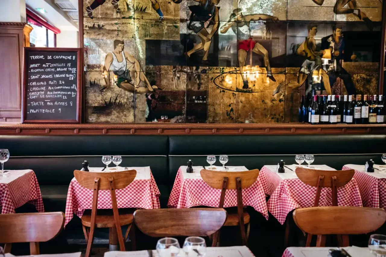Ambiance chaleureuse d'un **meilleur bistrot parisien** avec ses tables dressées, ses banquettes en cuir et sa fresque murale vintage.