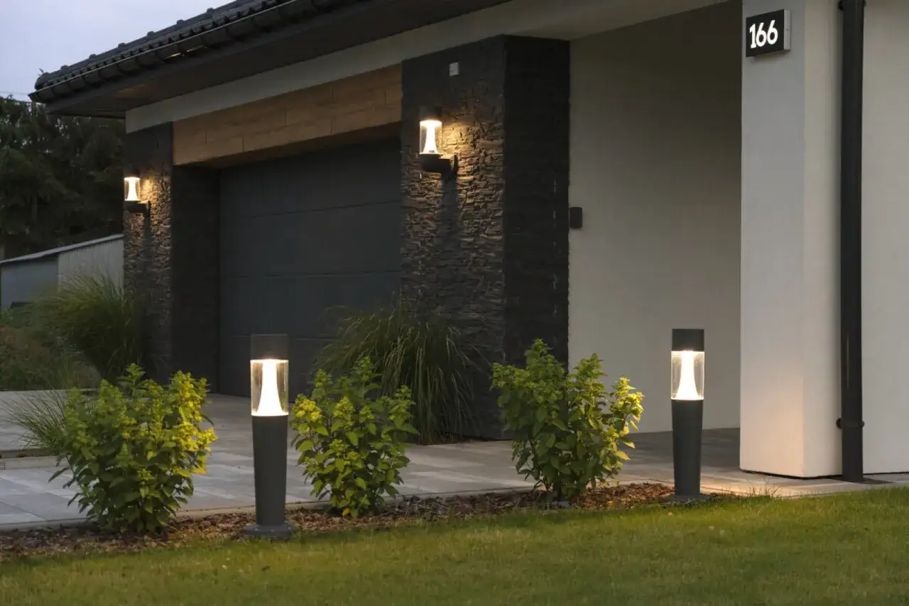 Nowoczesne lampy i kinkiety tworzą magiczną atmosferę, pokazując, jak oświetlić ogród. Elegancka elewacja i podjazd.