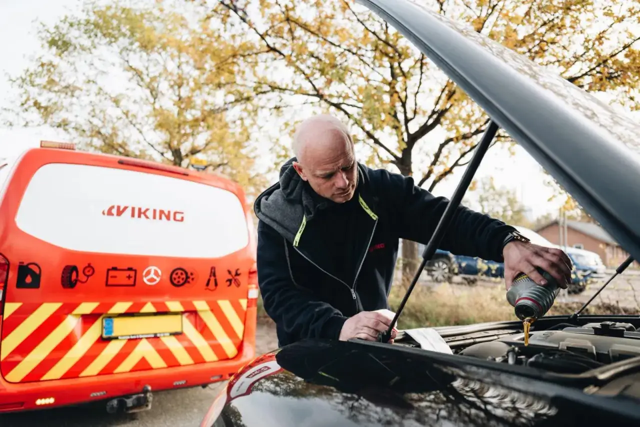 Man häller motorolja i bilen. Viking-bilen står bredvid, redo att hjälpa till med din motorolja guide.