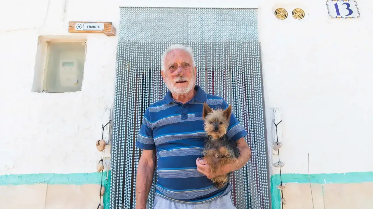 Un hombre mayor con un perro yorkshire en brazos, frente a una cortina de cuentas. Mi perro no ladra, pero me acompa&ntilde;a siempre.