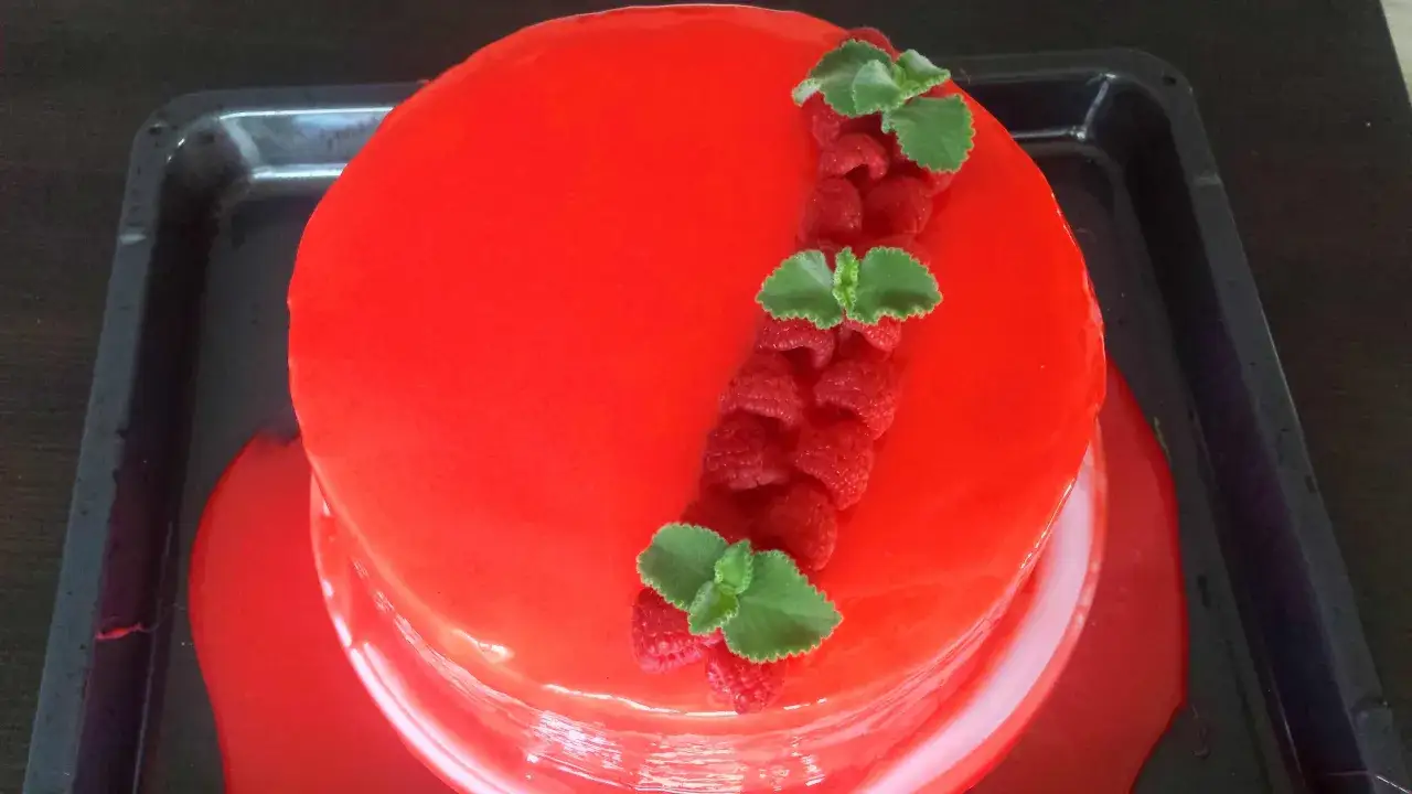 Lśniąca, czerwona glazura na tort, ozdobiona malinami i listkami mięty. Wygląda apetycznie!