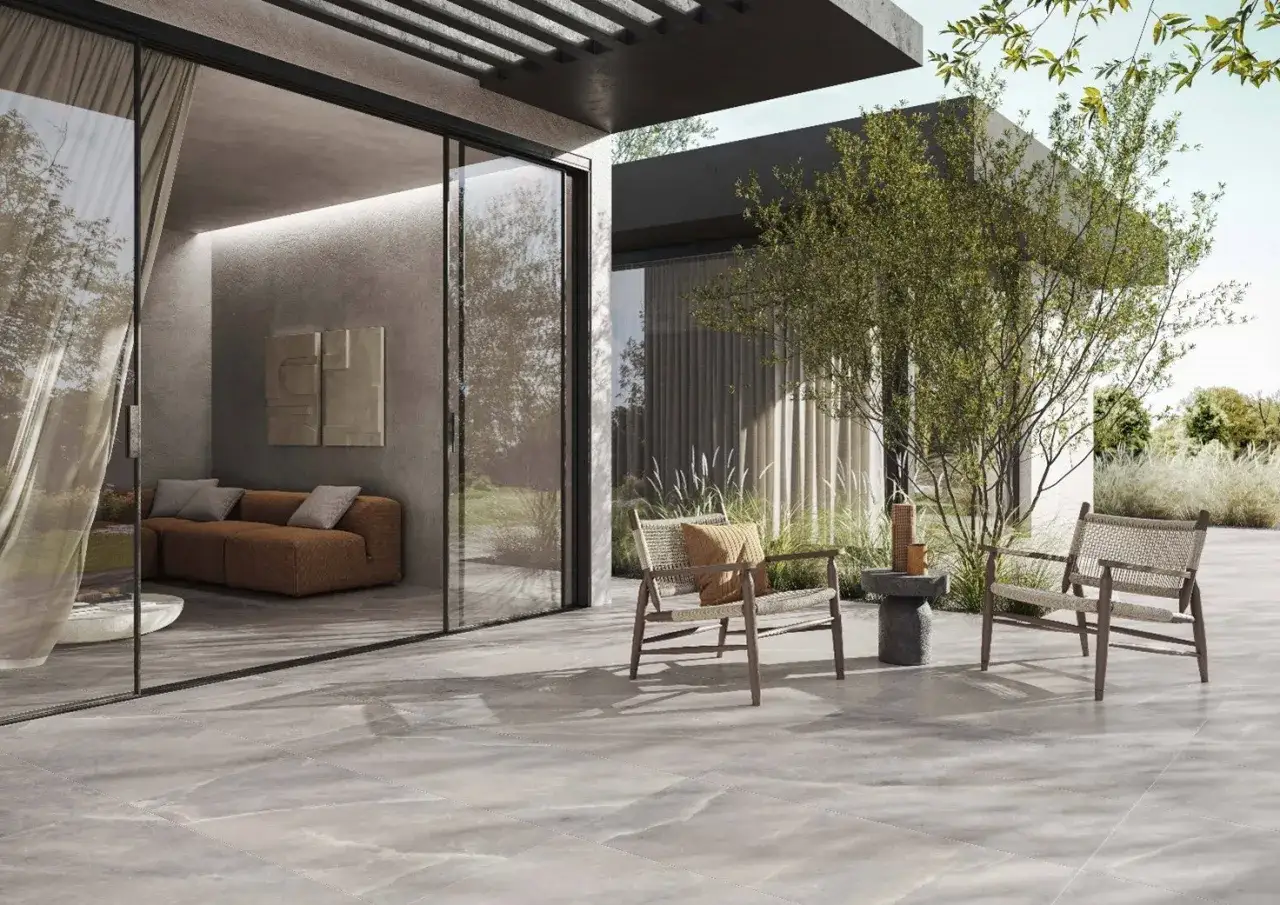 Terrazza moderna con pavimentazione in gres effetto pietra, due sedie in legno e un divano visibile all'interno.