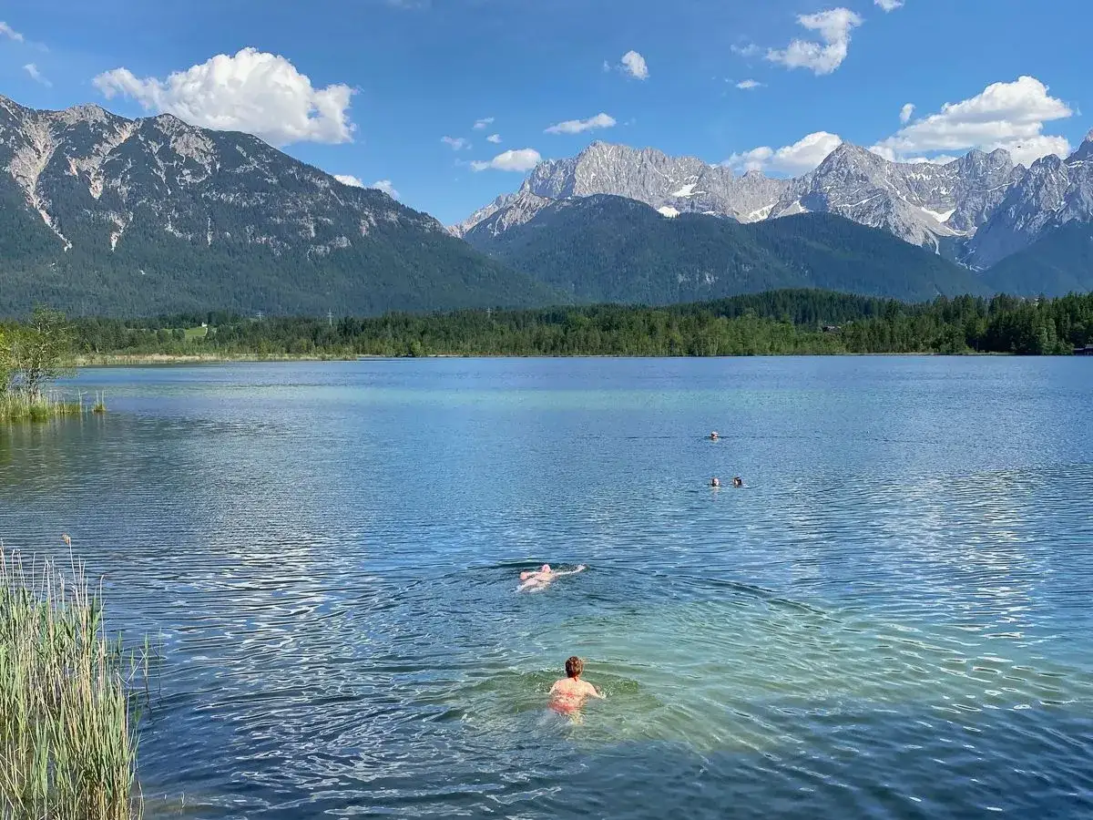 Schwimmer genie&szlig;en einen sonnigen Tag am See in Bayern, mit majest&auml;tischen Bergen im Hintergrund.