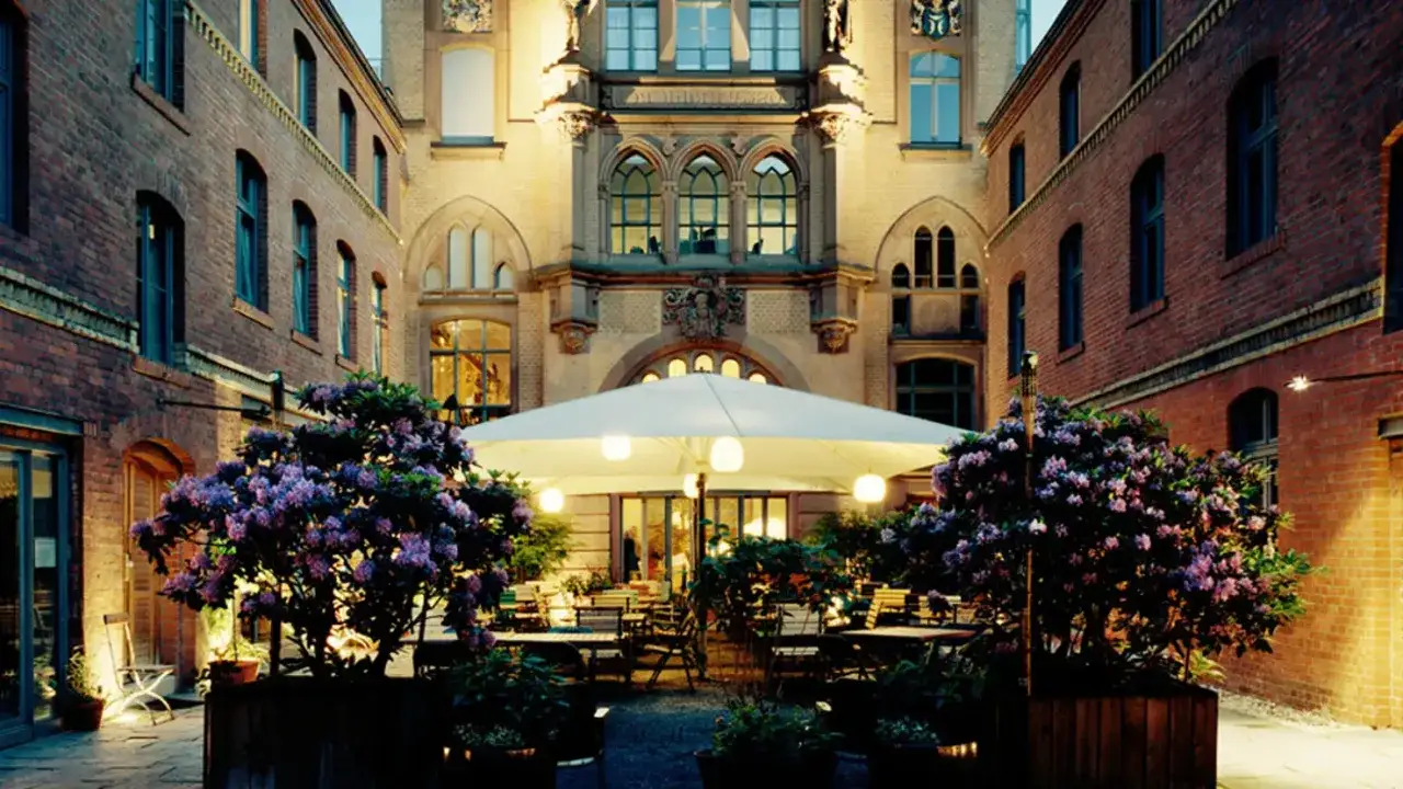 Ein lauschiger Innenhof mit blühenden Rhododendren, Tischen unter einem großen Sonnenschirm und historischer Backsteinarchitektur – ein echter Berlin Restaurant Geheimtipp.