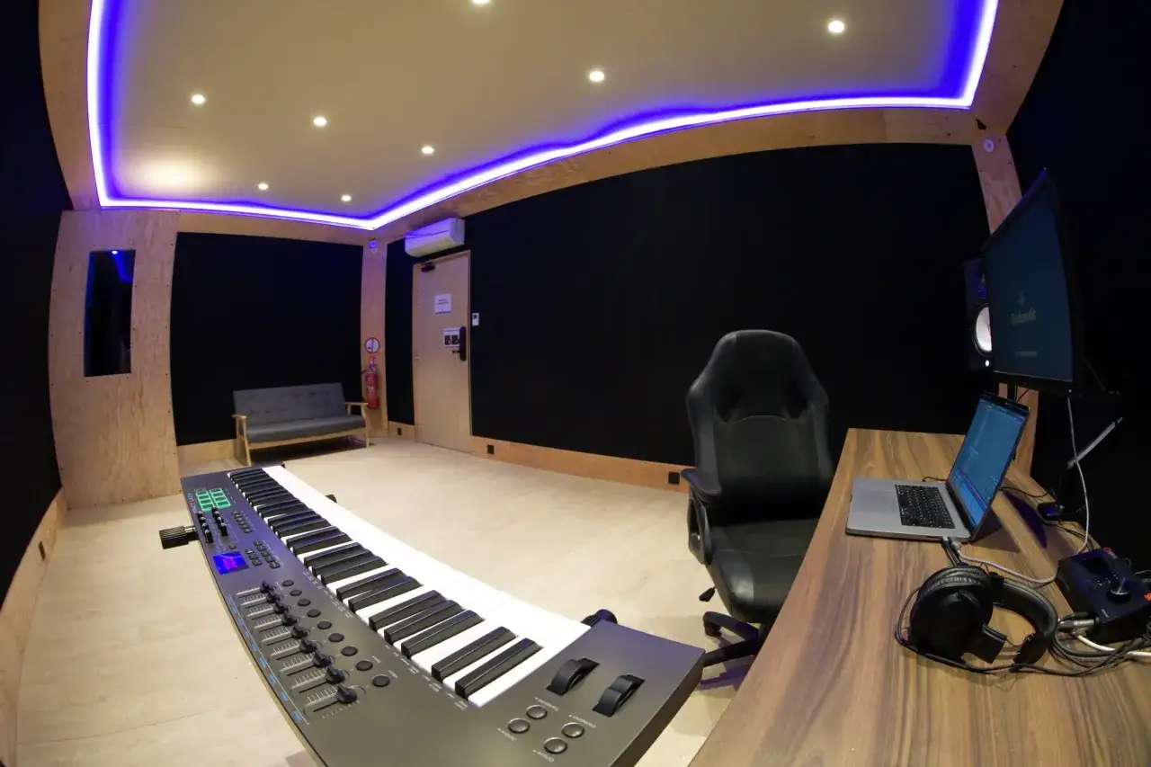 Studio d'enregistrement moderne avec clavier, ordinateur, casque et éclairage LED bleu, idéal pour la musique créative.