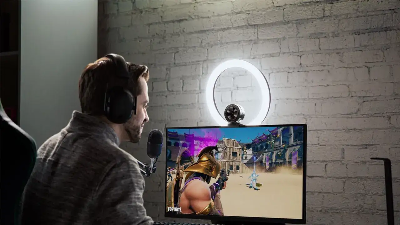 Un joueur avec casque et micro est prêt pour son setup streamer. Il joue à Fortnite devant un écran éclairé par un ring light.