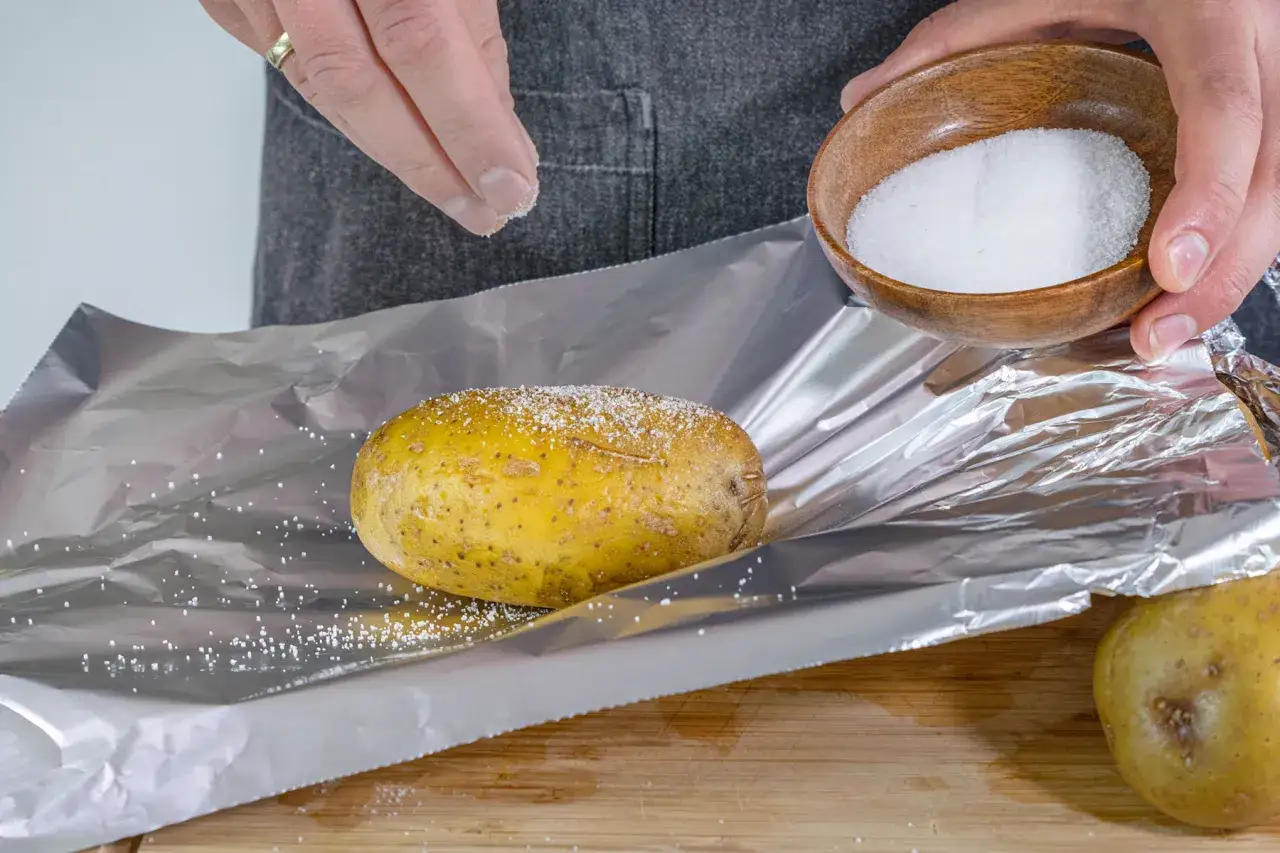 Salz wird auf eine Kartoffel gestreut, die auf Alufolie liegt. So werden die Kartoffeln vorkochen.