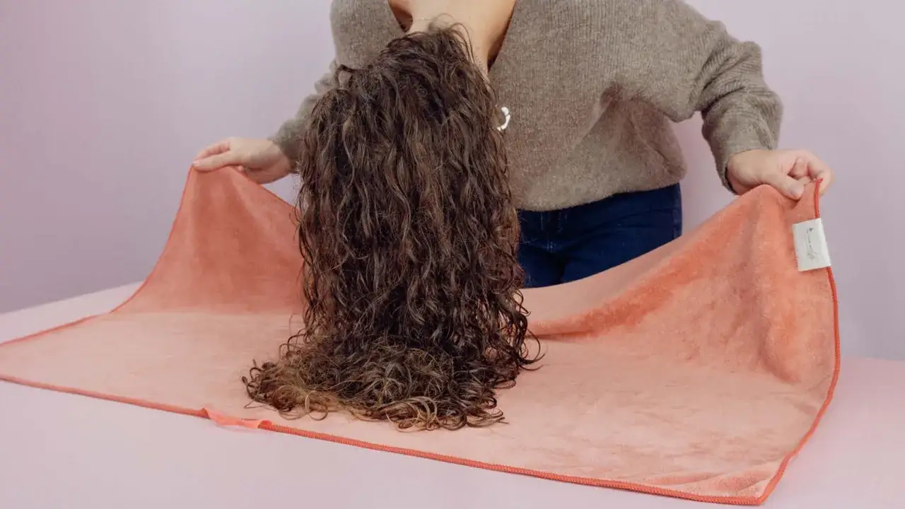 Une personne incline la tête, laissant tomber ses cheveux essorés sur une serviette corail.