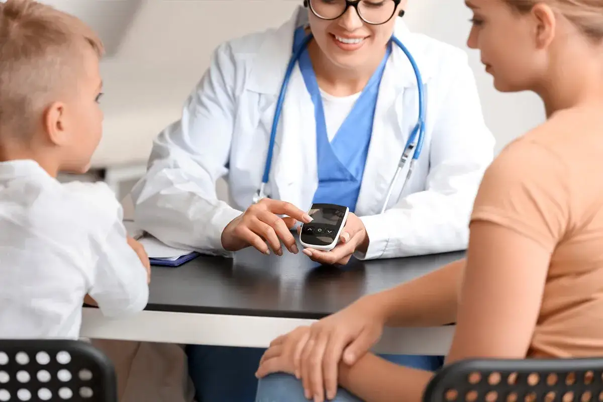 Medico mostra a madre e figlio un glucometro. Il diabete nei bambini si guarisce con cure adeguate e supporto.