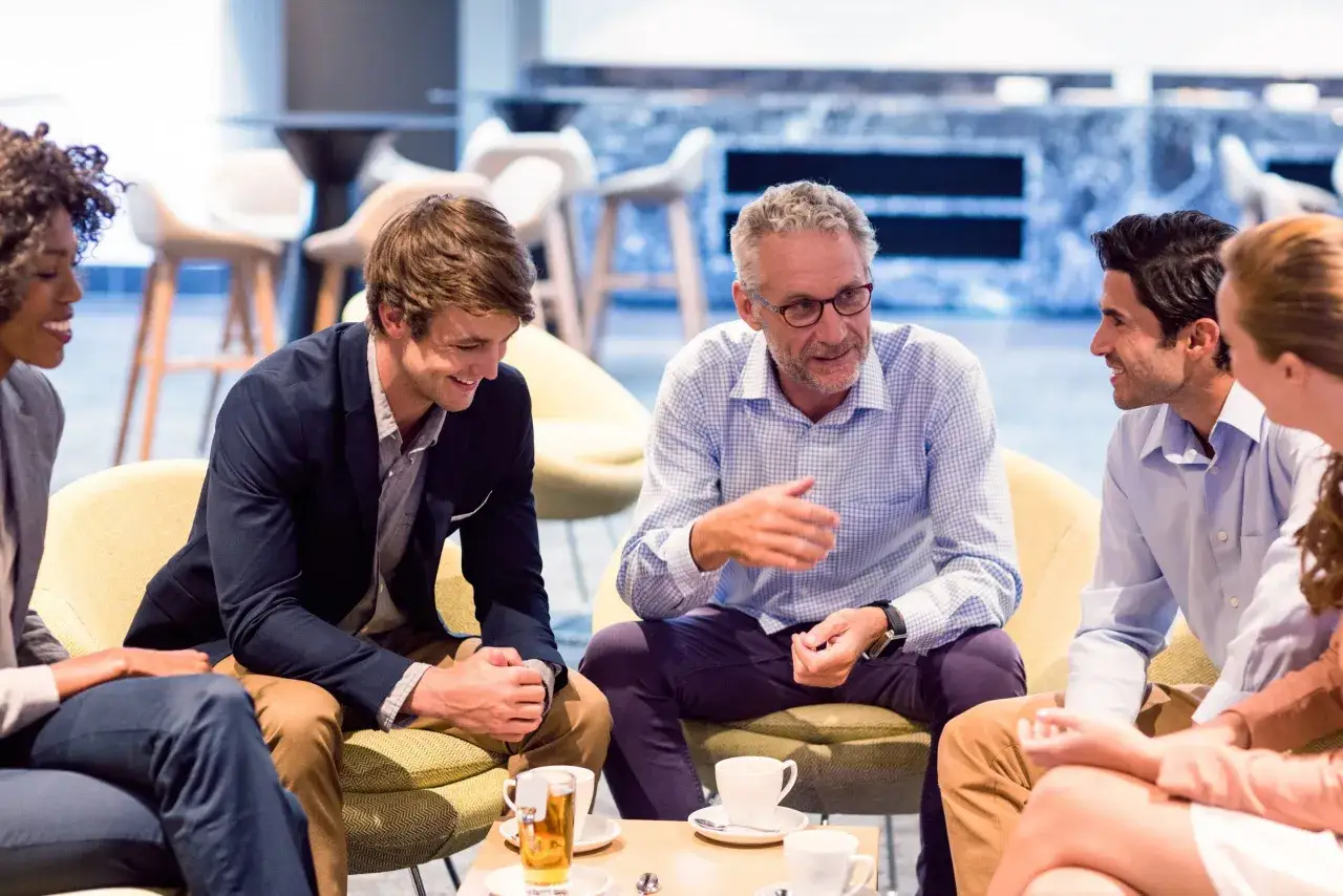 Diverse group engaged in a lively discussion, likely part of a leadership development program, sharing ideas over coffee.