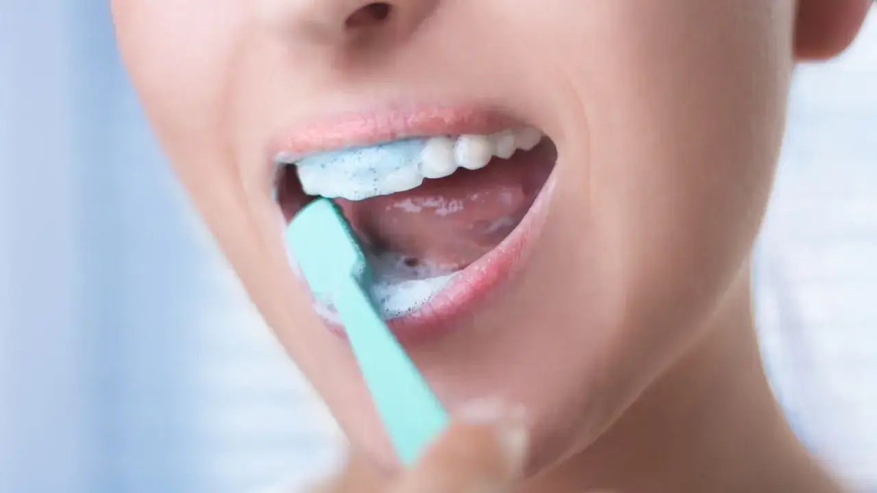 Close-up van een mond die tandenpoetst met een mintgroene tandenborstel en schuim, wat suggereert dat tandenpoetsen zonder tandpasta mogelijk is.