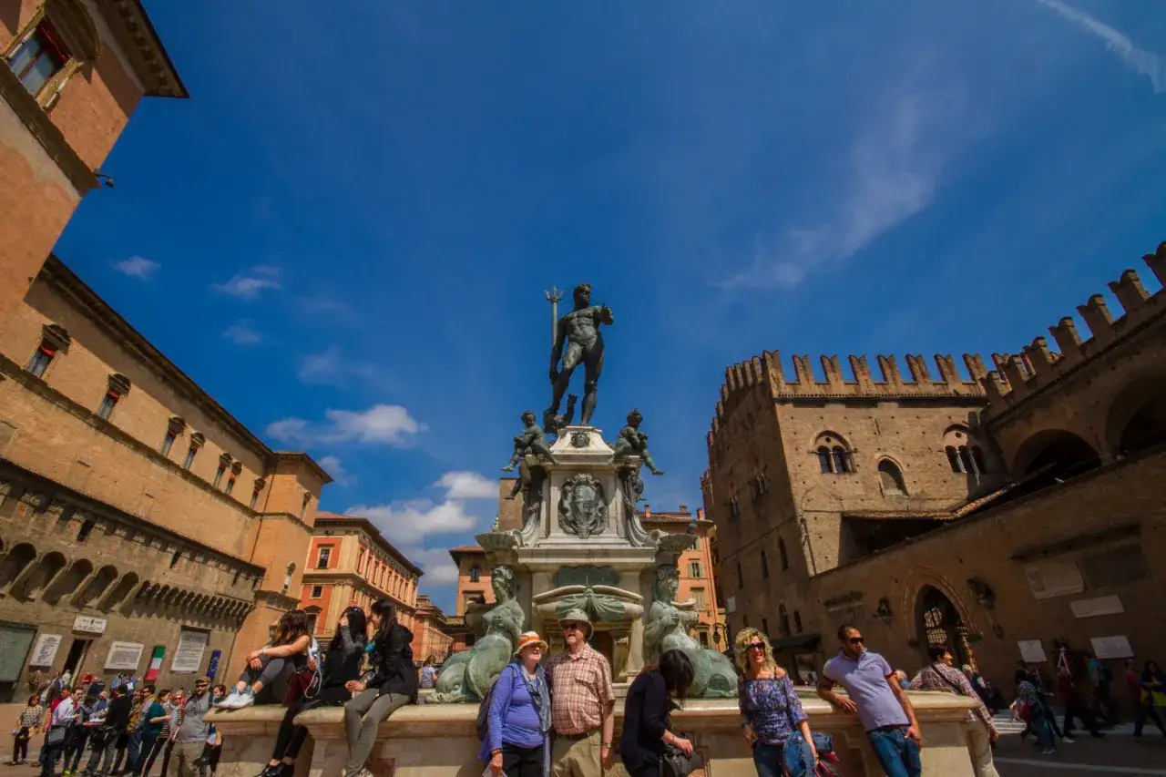 Fontana del Nettuno e palazzi storici in Piazza Maggiore, Bologna, con turisti che si godono la giornata.