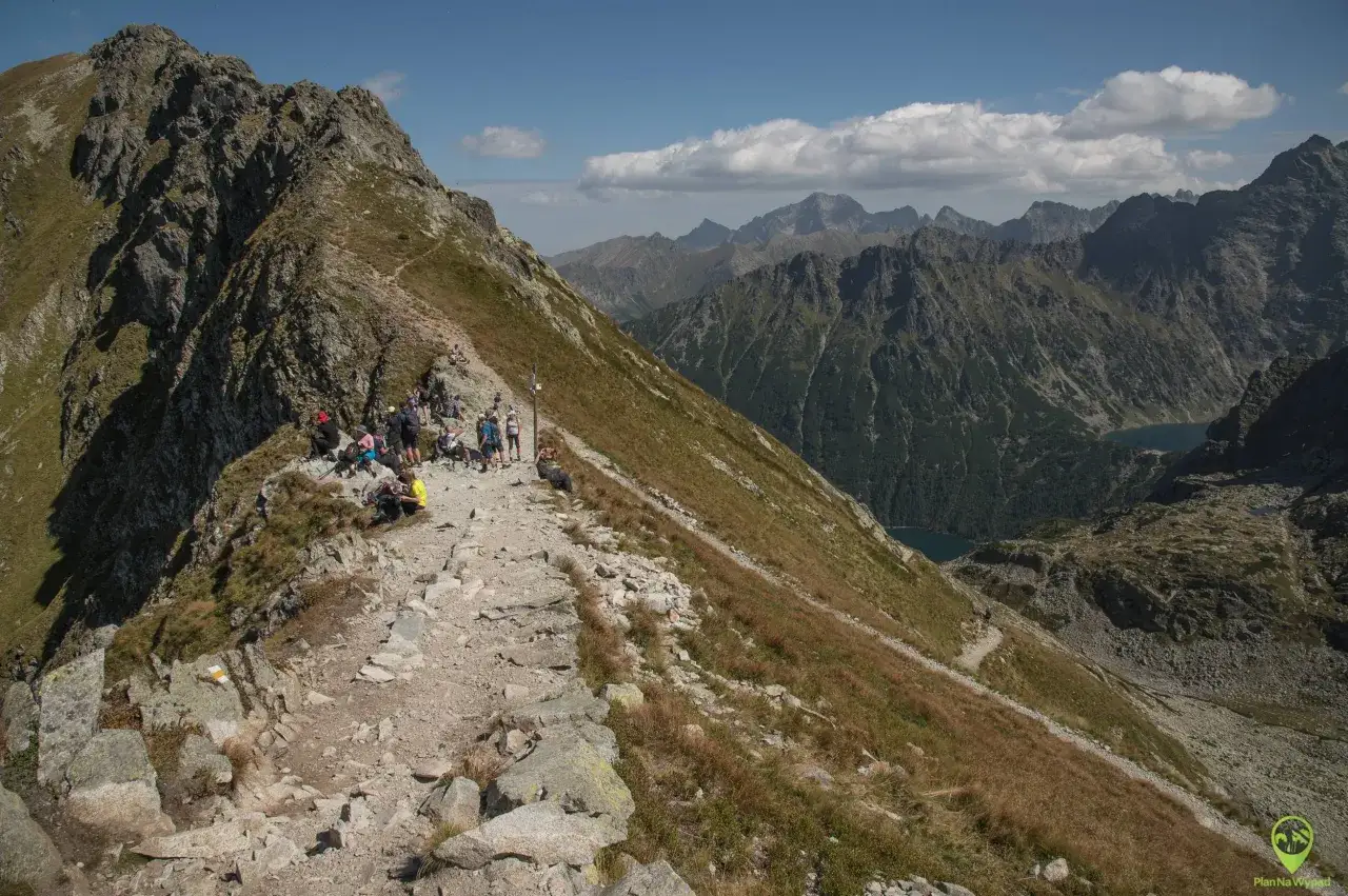 Szlak na Szpiglasowy Wierch. Grupa turystów odpoczywa na kamienistej ścieżce, podziwiając malowniczą, górską panoramę.