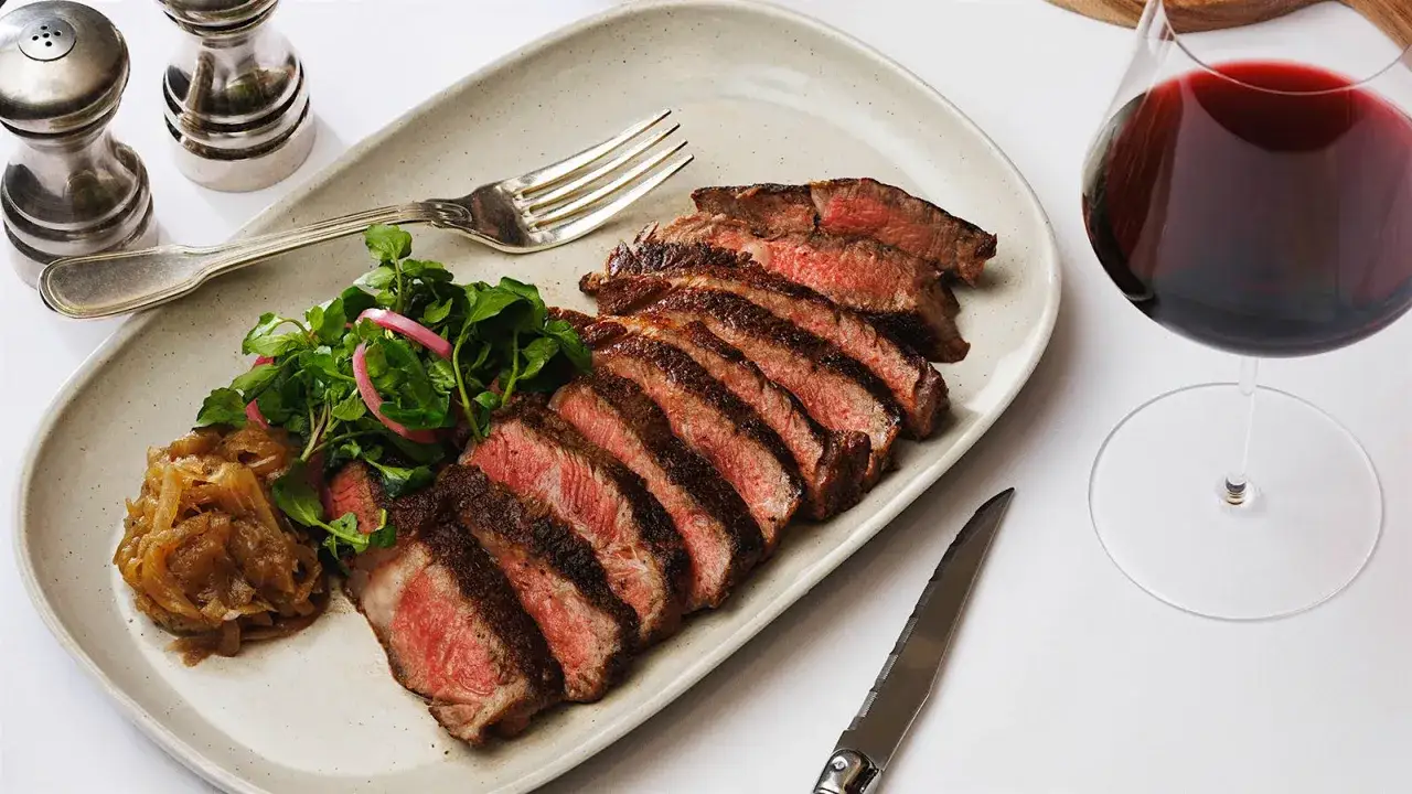En perfekt tillagad tagliata med sallad och karamelliserad lök, ackompanjerad av ett glas fylligt rött vin.