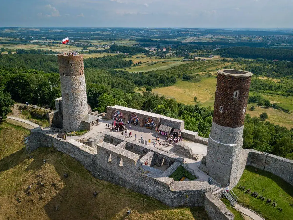 Zamek w Chęcinach z dwiema wieżami i polską flagą. Turyści zwiedzają ruiny. Sprawdź zamek Chęciny cennik przed wizytą.
