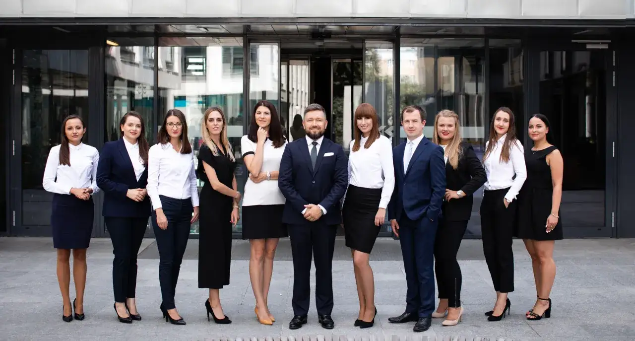 Grupa profesjonalistów w garniturach i sukienkach stoi przed nowoczesnym budynkiem.