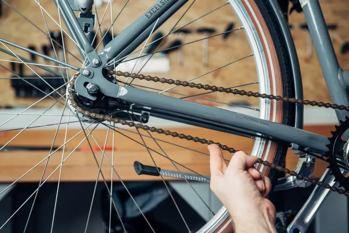 Hand pr&uuml;ft die Spannung der Fahrradkette an einem grauen Rad.