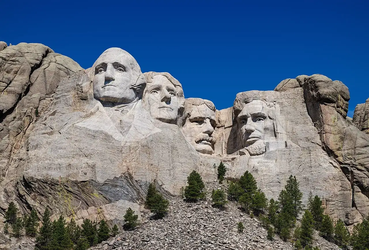 Las caras de cuatro presidentes de EE. UU. talladas en el **Monte Rushmore** bajo un cielo azul brillante.