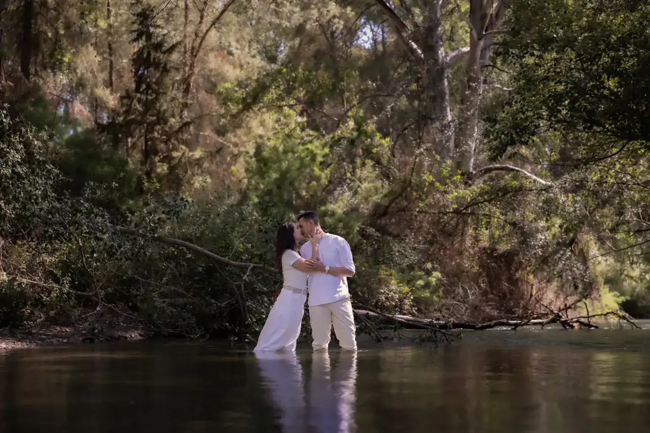 Pareja besándose en un río, disfrutando de su sesión preboda entre árboles frondosos.