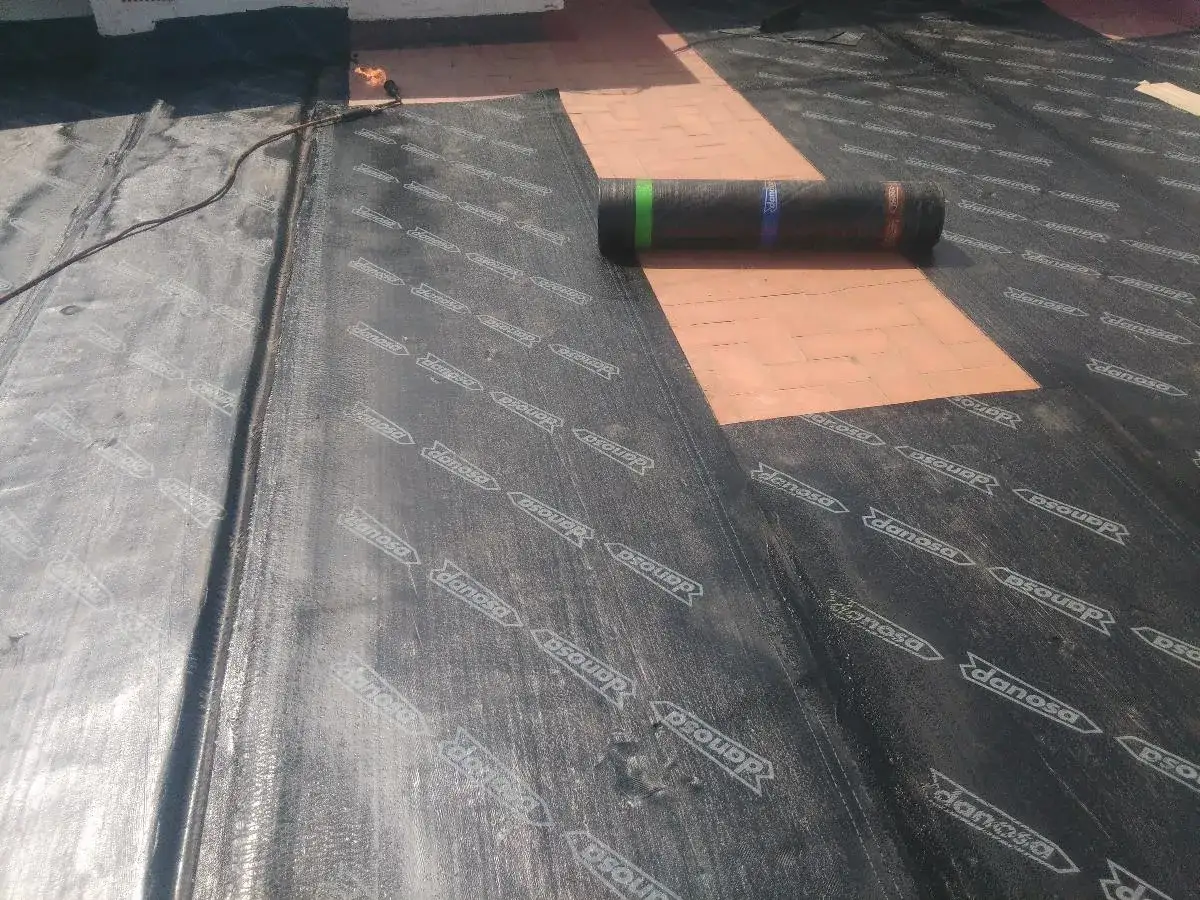 Instalaci&oacute;n de aislamiento t&eacute;rmico para terrazas transitables. Se ve una membrana negra con el logo 