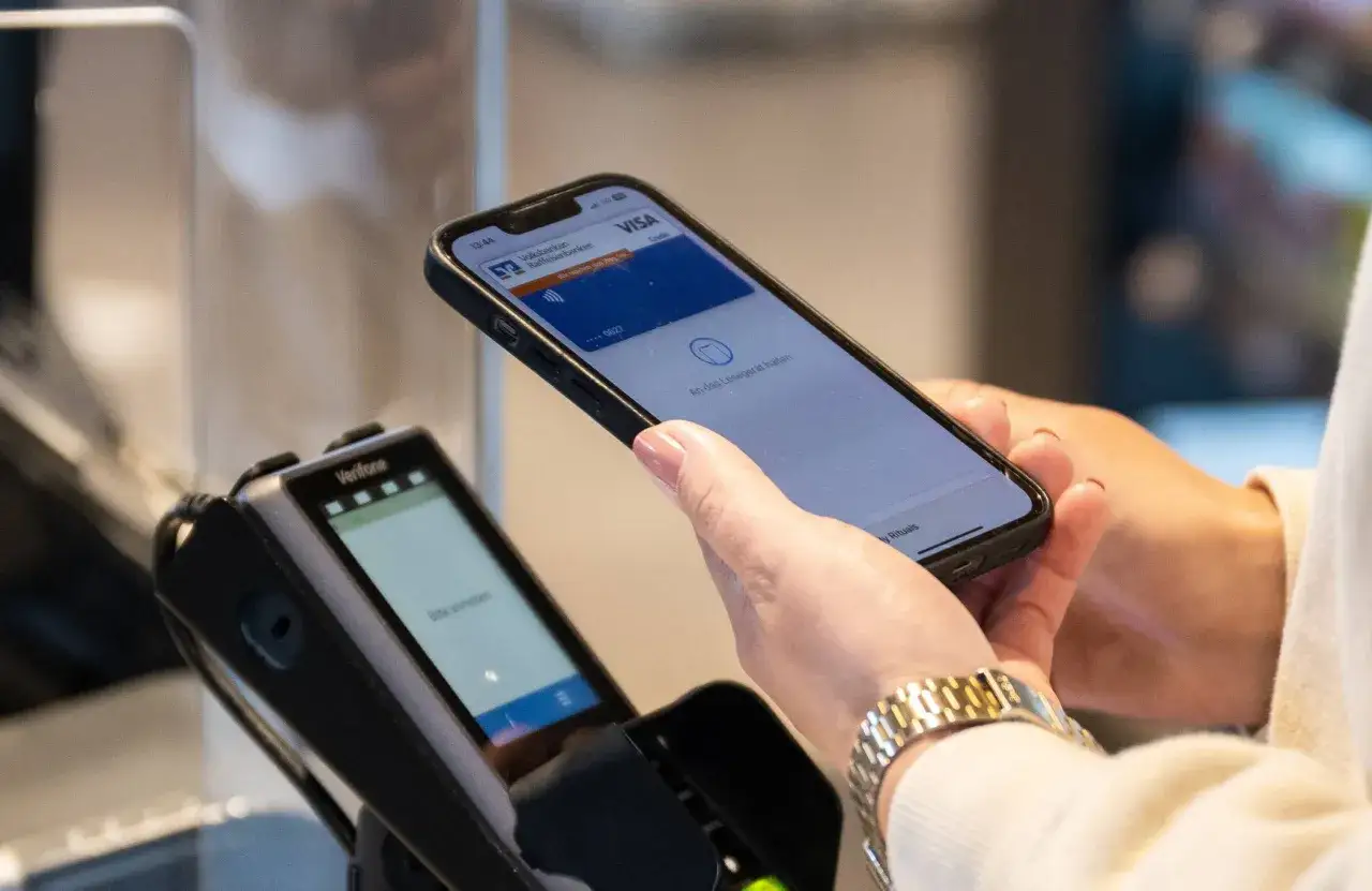 Eine Frau hält ihr iPhone mit Apple Pay an ein Terminal. So einfach funktioniert Apple Pay.