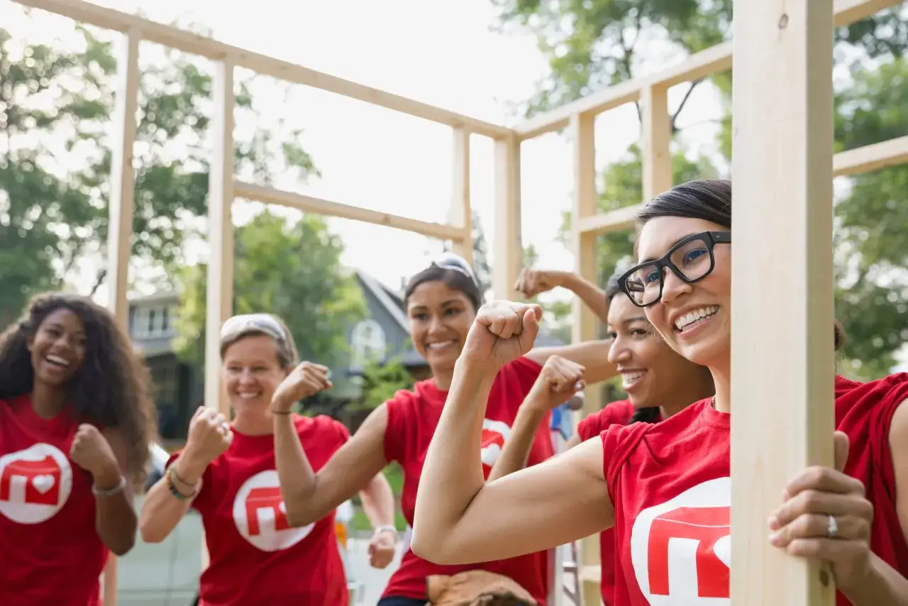 Women in red shirts flex muscles, showing teamwork and community spirit. Great staff retreat ideas for nonprofits involve hands-on projects like this.