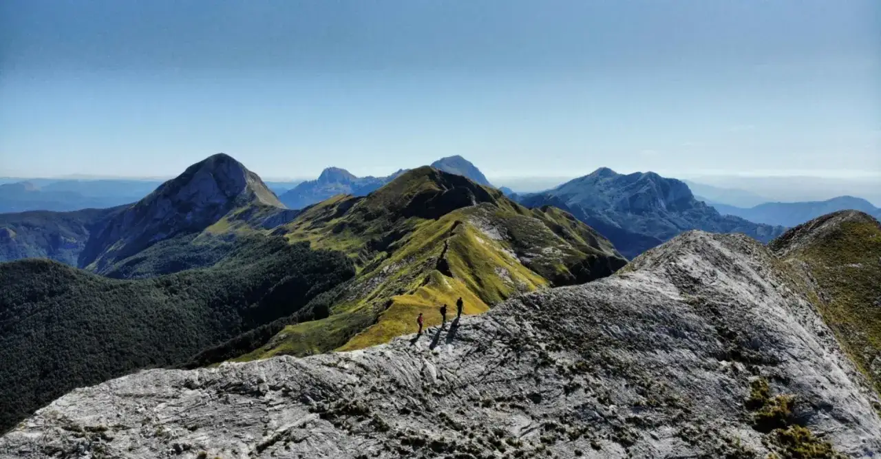 Trekking in **Garfagnana**, dove si trova questo panorama mozzafiato con vette verdi e rocciose sotto un cielo azzurro.