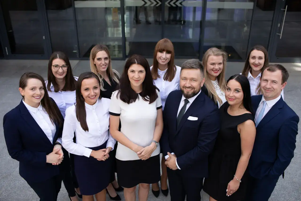 Grupa prawników i radców prawnych w formalnych strojach stoi przed budynkiem.