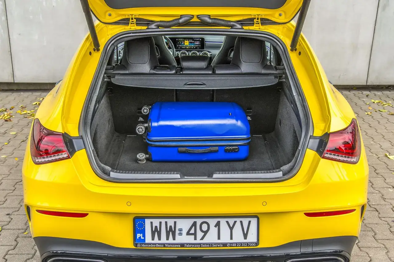 Żółty CLA shooting brake gotowy na podróż. W bagażniku zmieści się niebieska walizka.