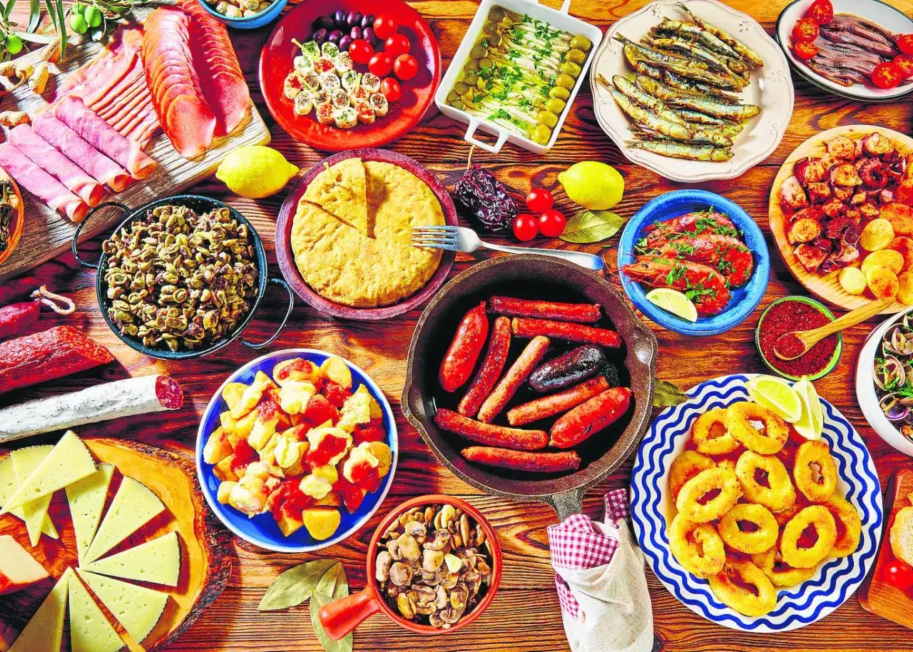 Mesa llena de pinchos y tapas originales: tortilla, salchichas, calamares, gambas, boquerones, queso y embutidos. ¡Un festín!