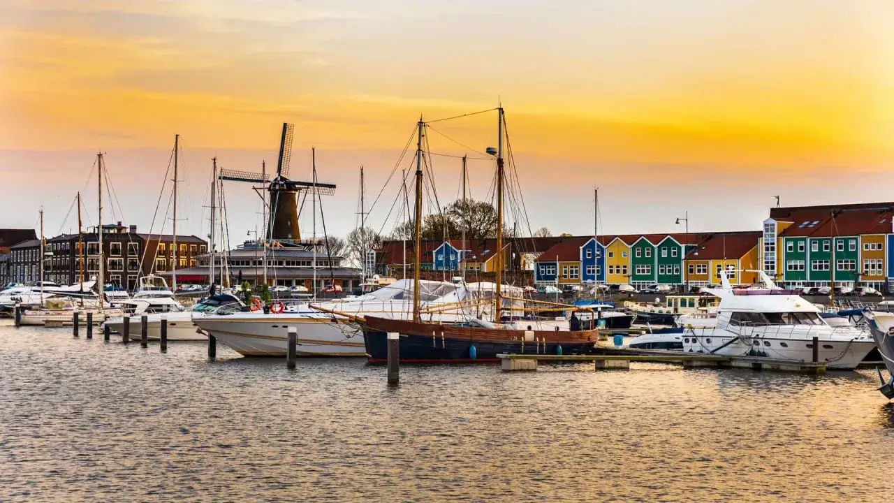 Bunte Häuser und ein historischer Windmühle säumen den lelystad hafen, wo Yachten und Segelboote im goldenen Abendlicht ruhen.
