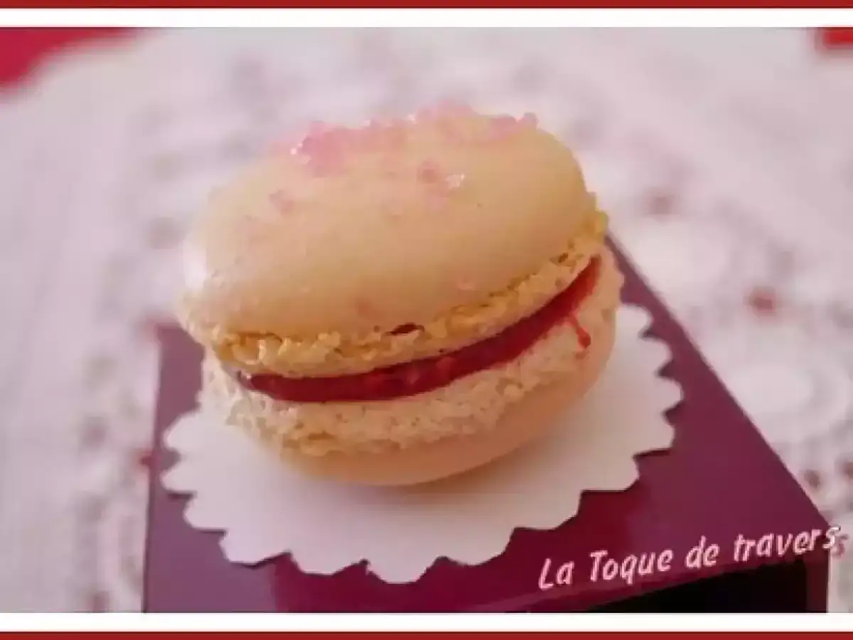 Macaron vanille garni d'une ganache fraise et saupoudré de sucre rose.
