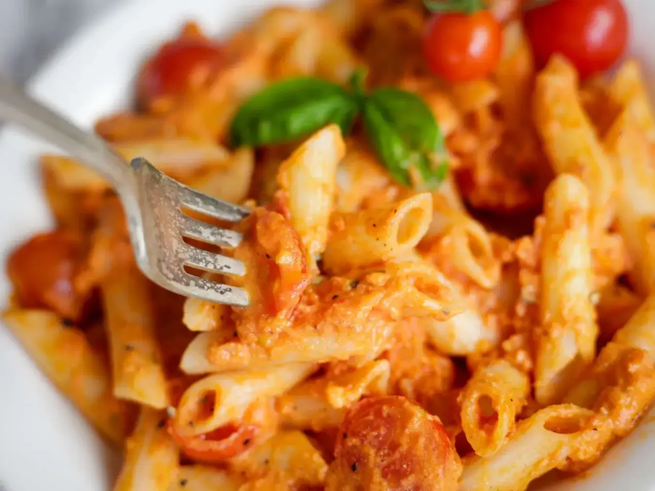 En gaffel lyfter en tugga av krämig vodka pasta med körsbärstomater och basilika.