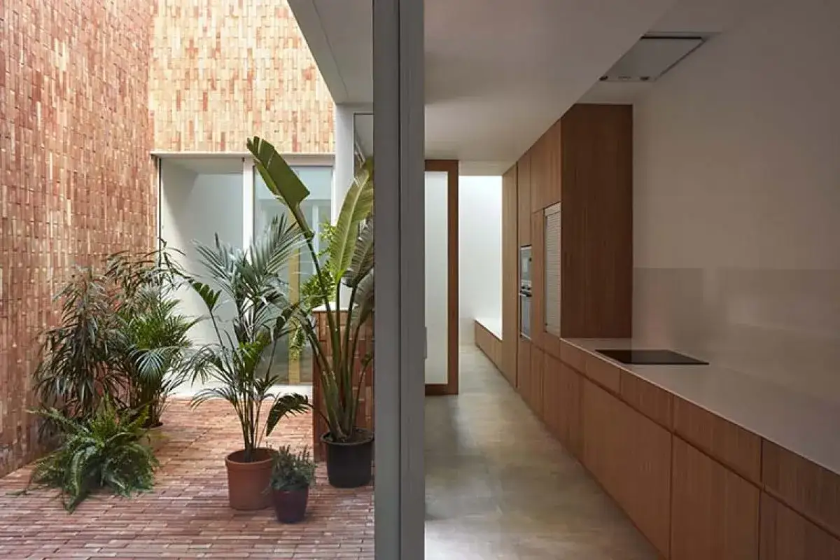 Un patio interior con plantas exuberantes y paredes de ladrillo se une a una cocina moderna con gabinetes de madera. Una **casa antigua** renovada con estilo.