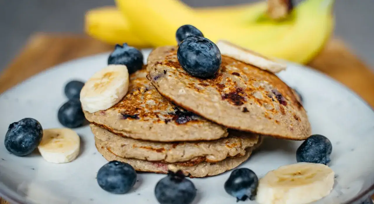 En hög med bananpannkakor, toppad med blåbär och bananskivor. Ett perfekt bananpannkaka recept för en god frukost.