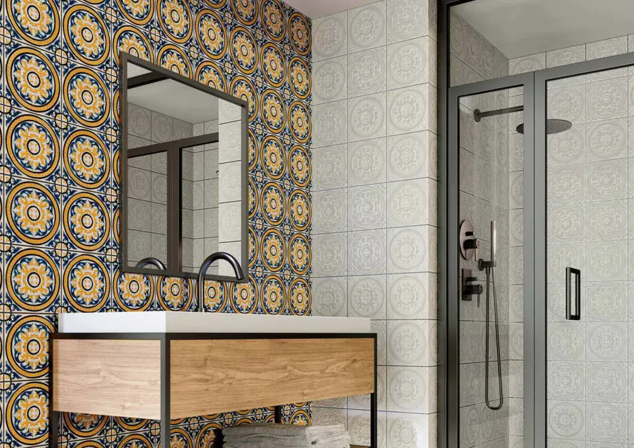Ba&ntilde;o peque&ntilde;o con azulejos de estilo hidr&aacute;ulico en azul y amarillo vibrante en una pared, y azulejos blancos con relieve en otra.