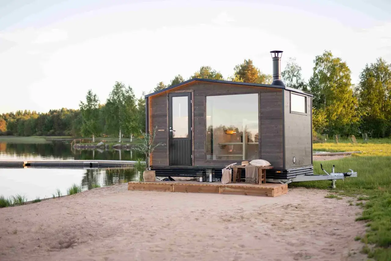En m&ouml;rk tr&auml;bastu p&aring; hjul vid en sj&ouml;. Kanske kr&auml;vs bygglov f&ouml;r denna mobila bastu?