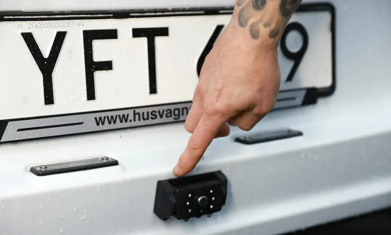 En hand pekar p&aring; en nyinstallerad backkamera under registreringsskylten.