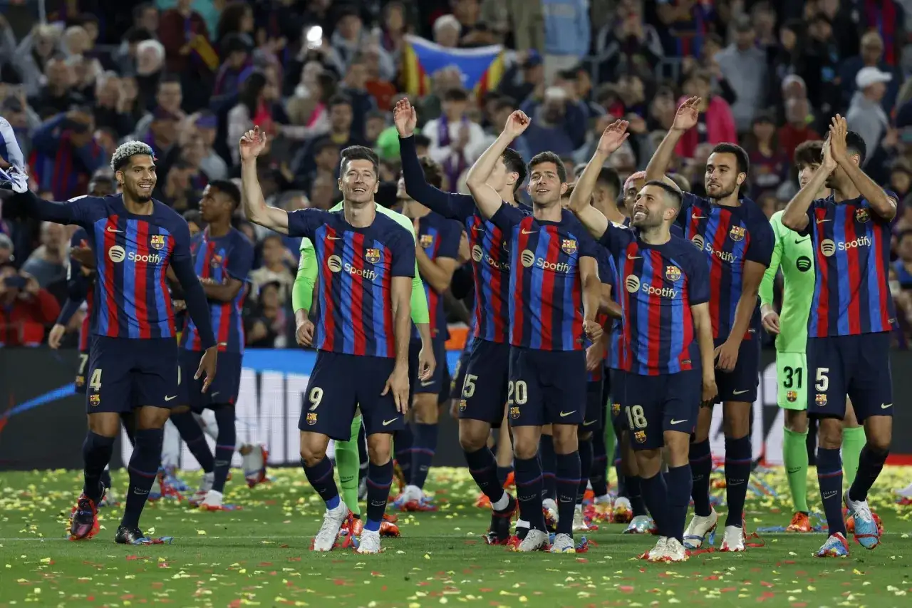 Piłkarze FC Barcelona w strojach z sezonu barcelona 22/23 świętują na murawie, wśród konfetti.