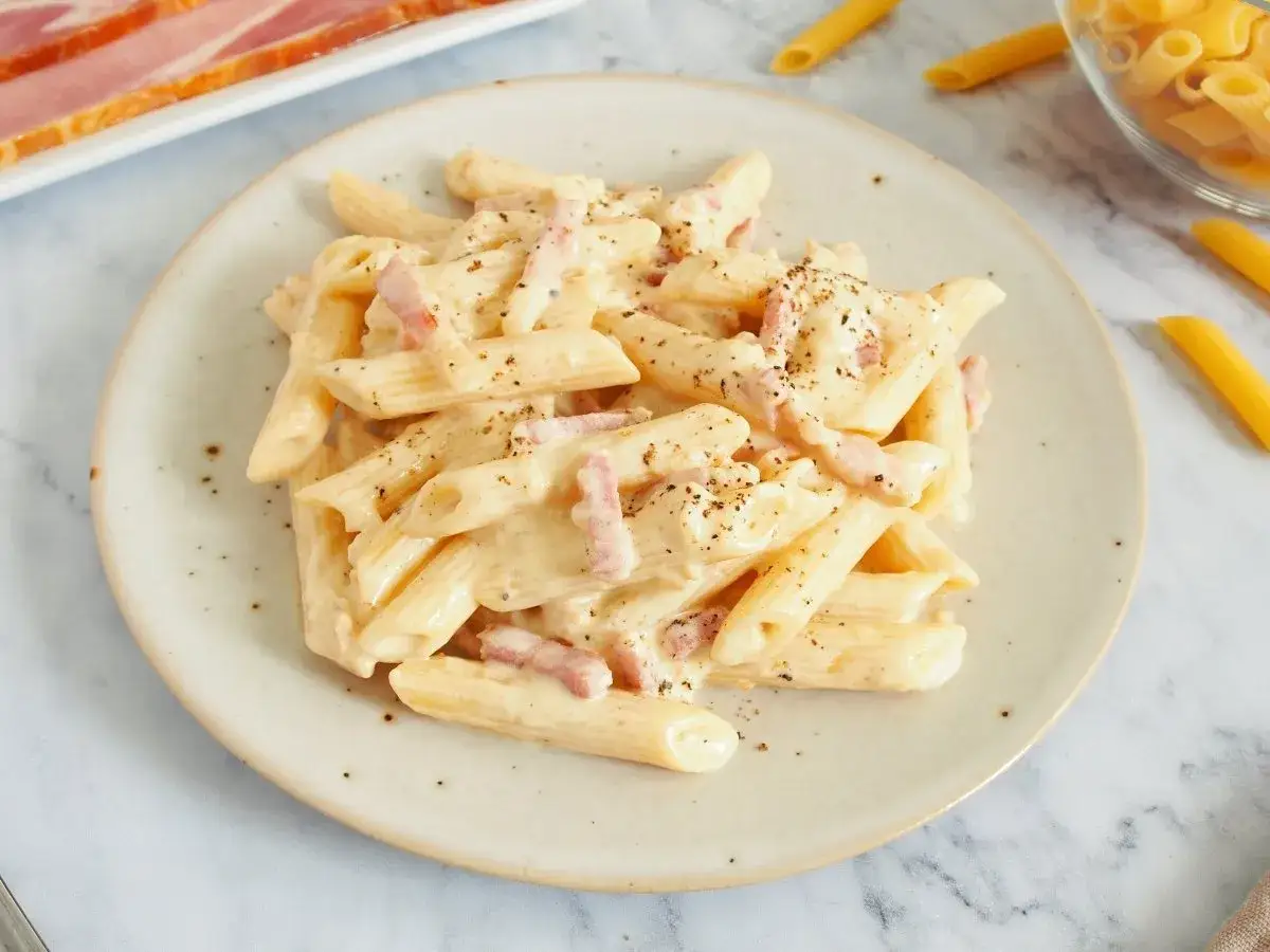 Plato de pasta penne cremosa con trozos de bacon crujiente y pimienta negra.