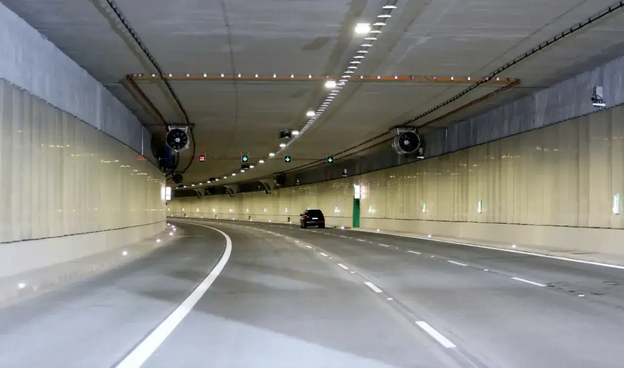 Wnętrze najdłuższego tunelu w Europie. Jedno auto jedzie pustą, oświetloną drogą.