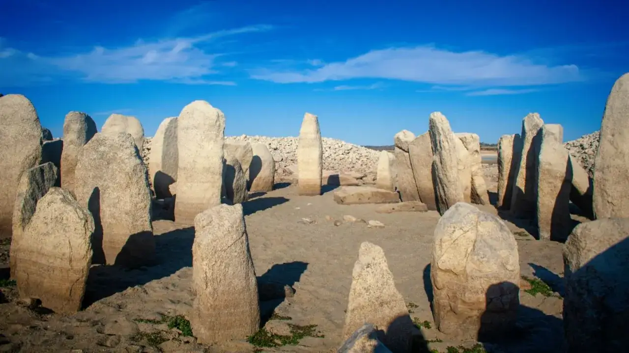 Antiguos megalitos en España emergen de la arena bajo un cielo azul, testigos silenciosos de la historia.