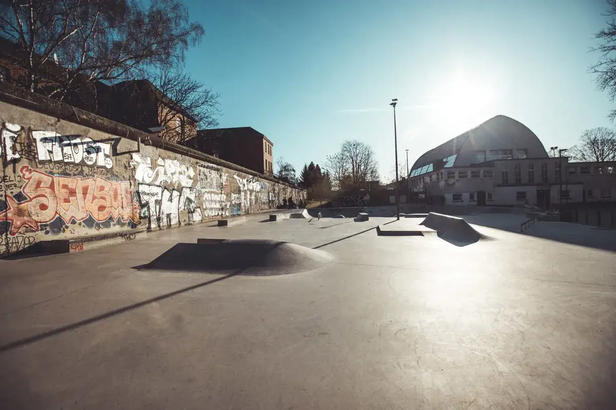 Sonniger Tag im **Berlin Skatepark**. Graffiti ziert die Mauer, w&auml;hrend Rampen und Rails auf Skater warten.