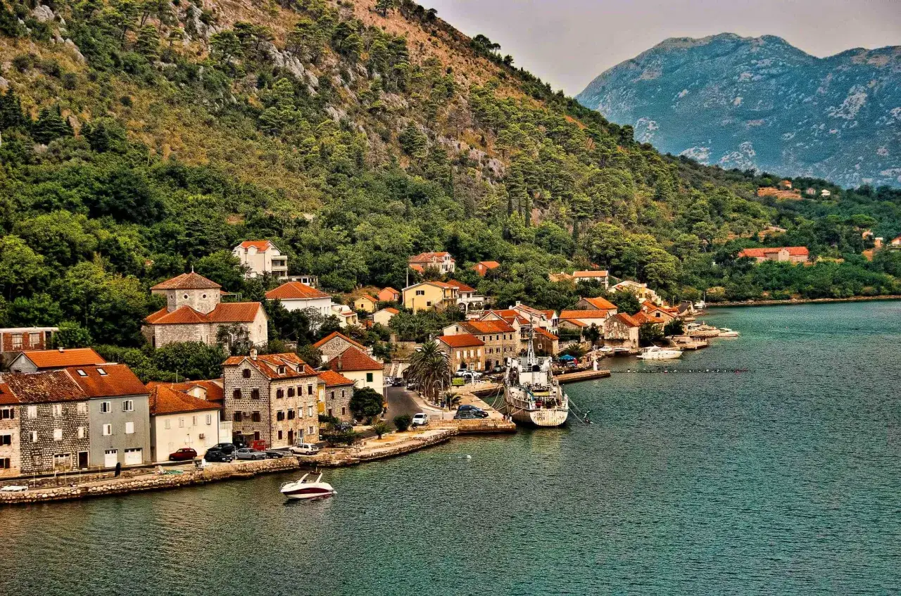 Blick aus der Drohne auf eine Küstenstadt in Montenegro mit roten Dächern, grünen Hügeln und blauem Wasser.