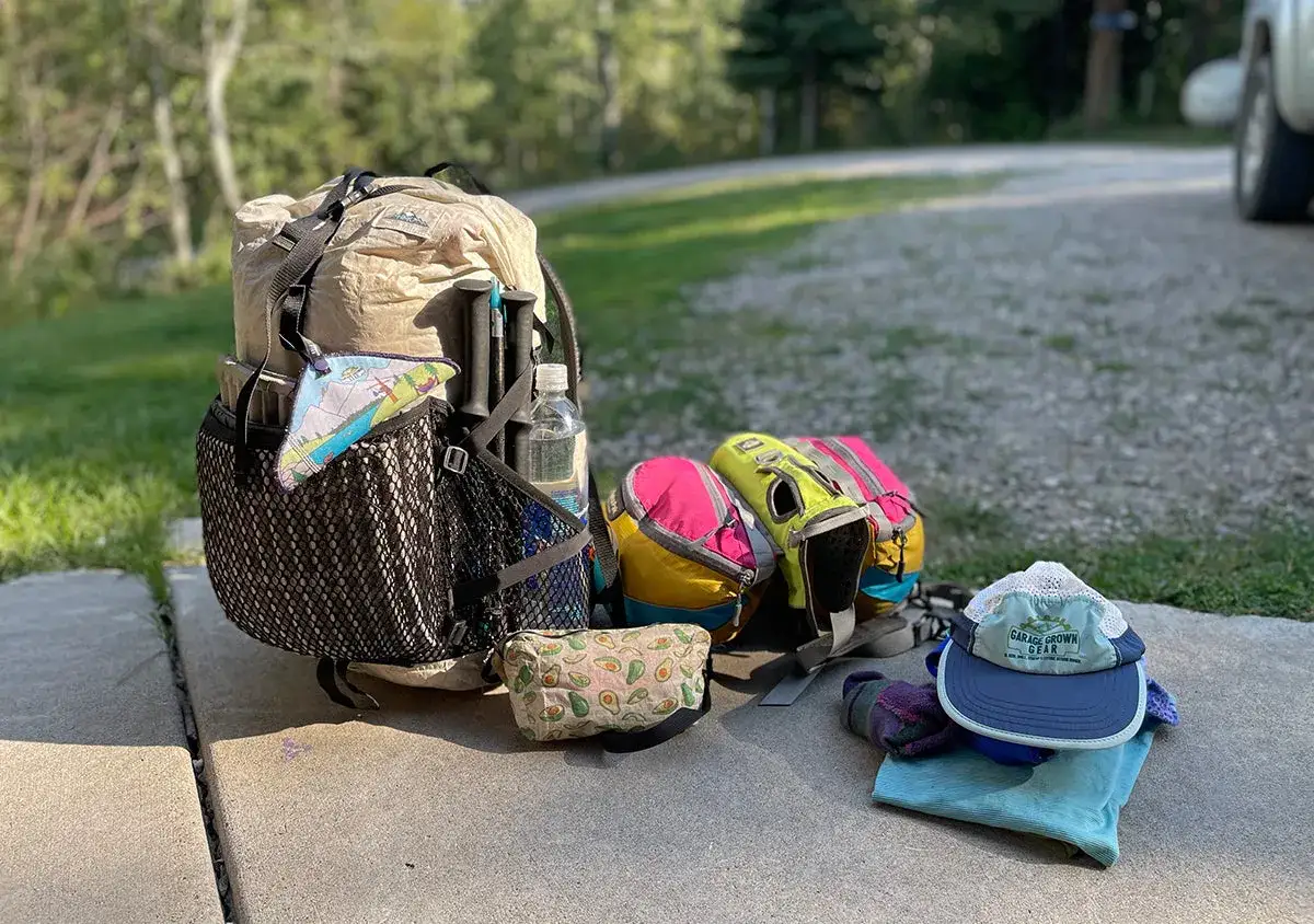 Pr&eacute;paration pour faire son sac de randonn&eacute;e &agrave; la journ&eacute;e : sac &agrave; dos, b&acirc;tons, gourde, sacs color&eacute;s, trousse et casquette.