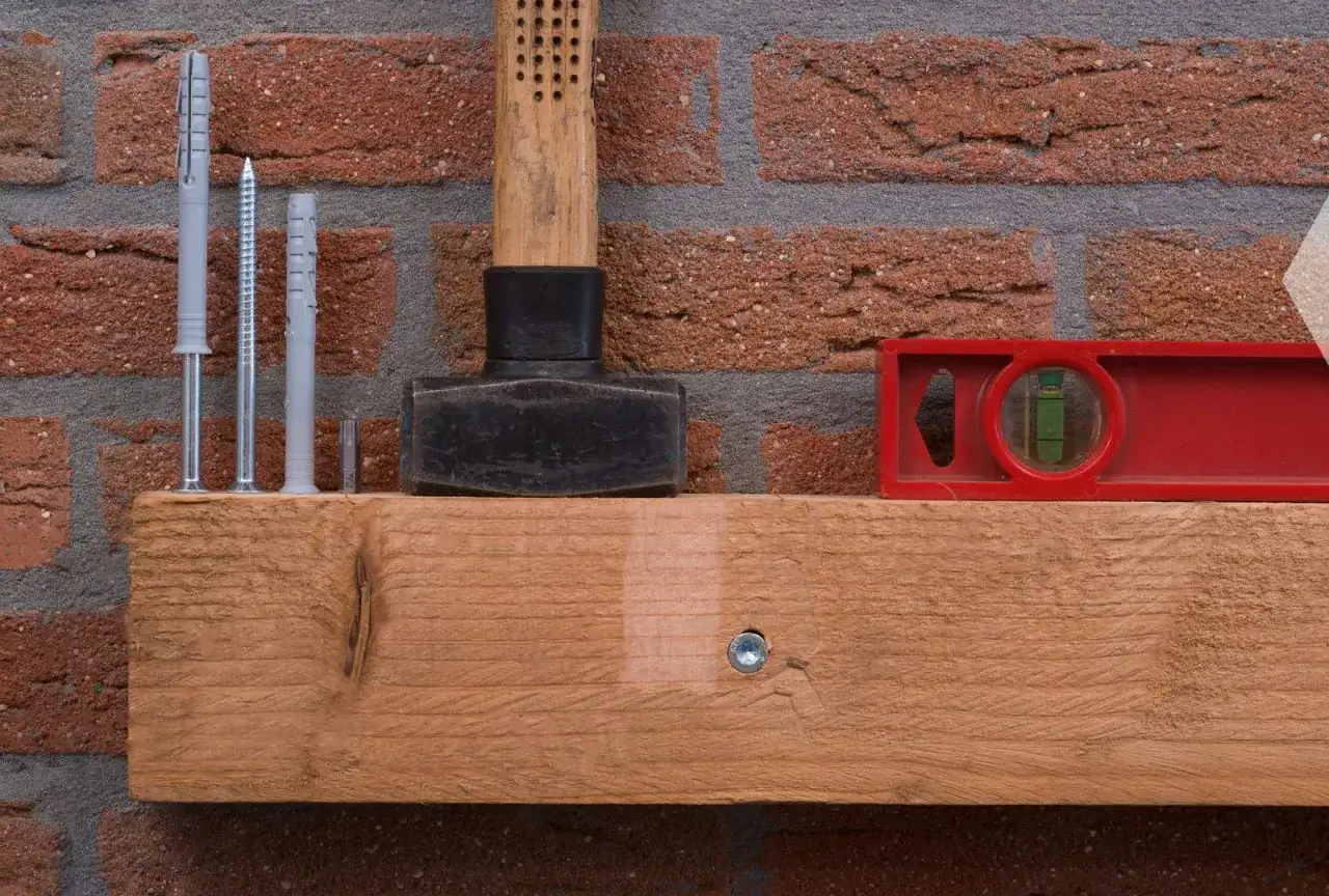 Werkzeugset zum Balken an Wand befestigen: D&uuml;bel, Schrauben, Hammer, Wasserwaage und Holzbalken vor Ziegelwand.