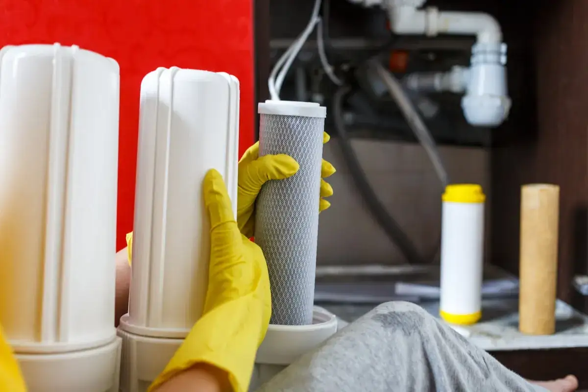 Mains de gants jaunes manipulant une cartouche de filtre à eau pour nettoyer la résine.