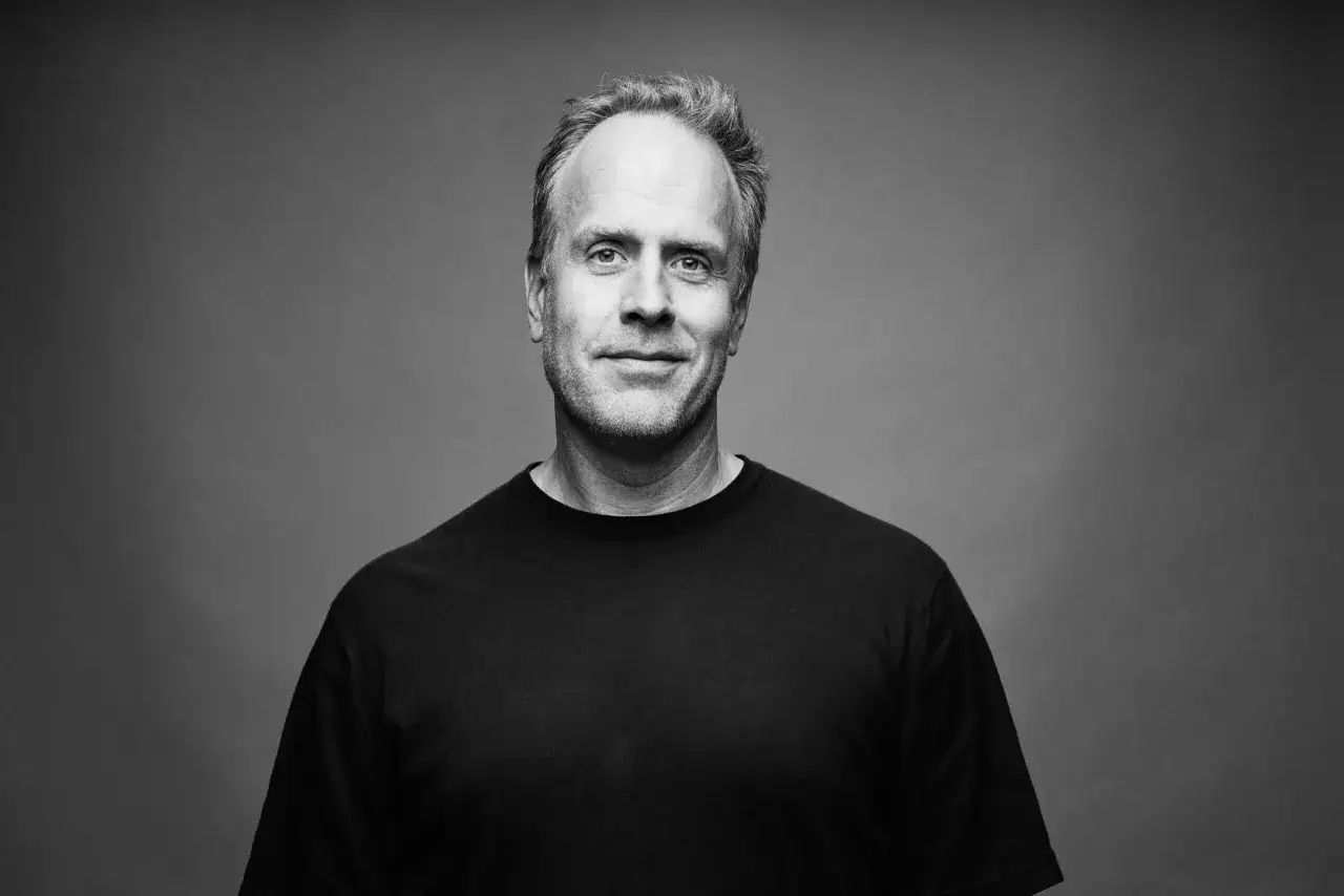 Porträtt av Magnus Lindqvist, en man med gråsprängt hår och ett vänligt leende, klädd i en svart t-shirt.