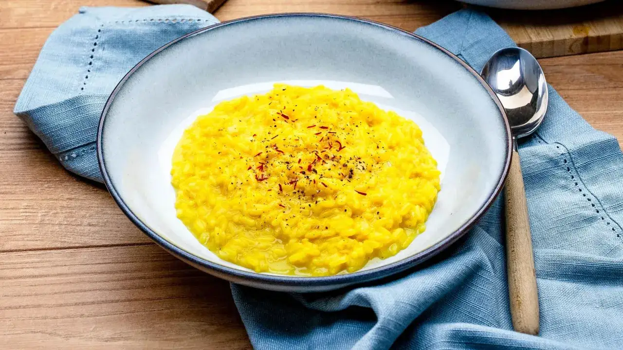 Cremiges Risotto Milanese, leuchtend gelb durch Safran, garniert mit feinen Safranfäden und schwarzem Pfeffer.